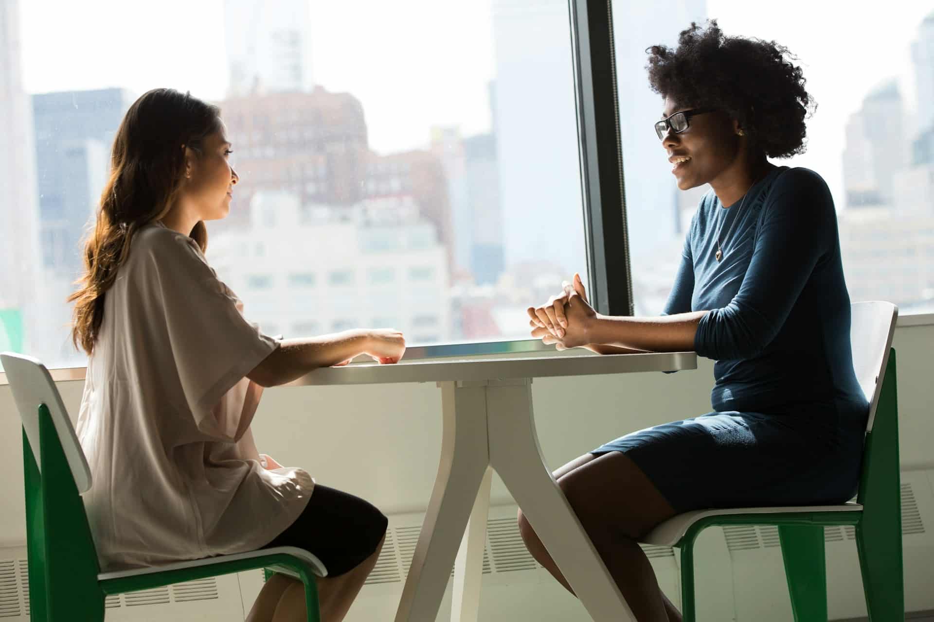 Two people talking at a table by a bright window